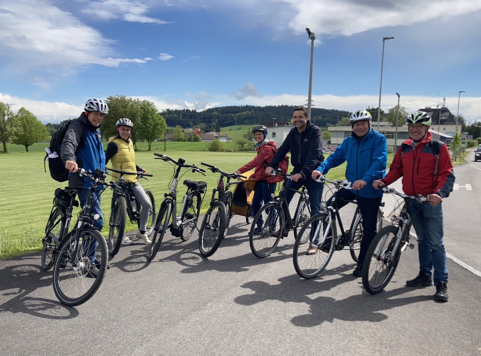 kleine Gruppe von Radfahrenden im Halbkreis aufgestellt in eher ländlicher Umgebung