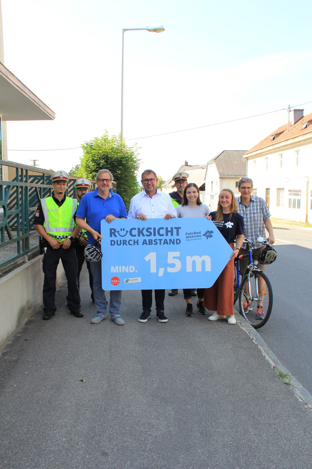 Eine Gruppe von Erwachsenen und 3 Polizisten präsentieren ein Plakat "Rücksicht durch Abstand - mind. 1,5m"