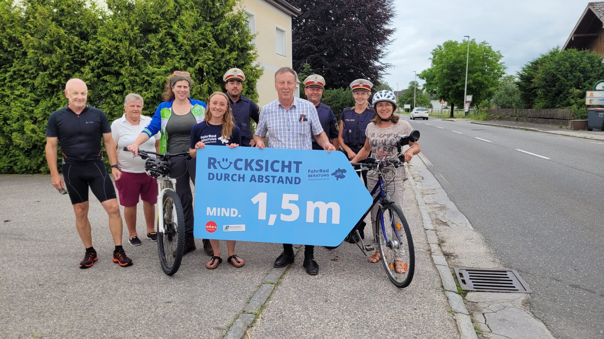 Eine Gruppe von Erwachsenen und 3 Polizisten präsentieren ein Plakat "Rücksicht durch Abstand - mind. 1,5m"