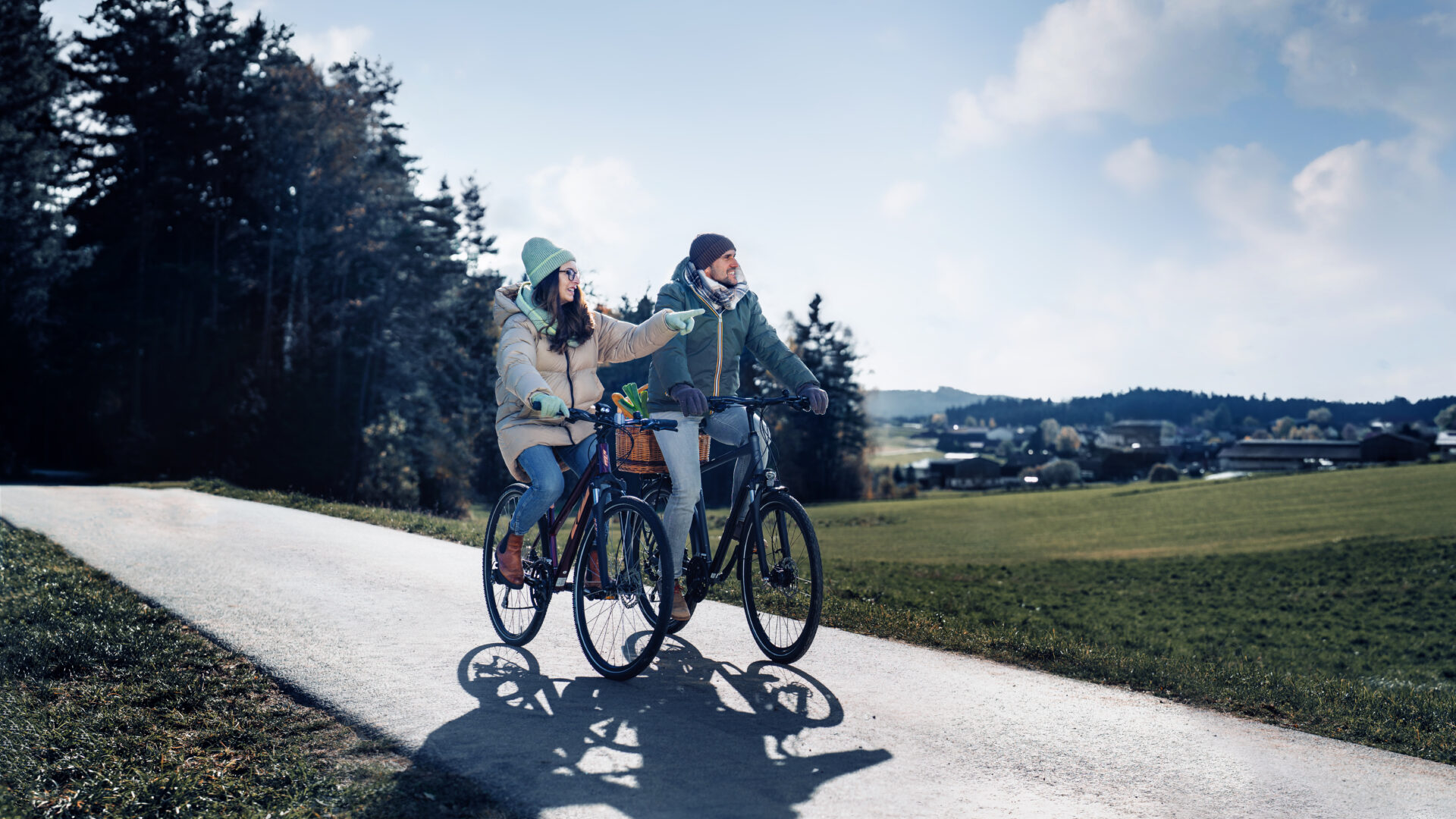Eine Frau und ein Herr radeln in der Natur. Die Frau zeigt mit dem Finger auf etwas in der Gegend.