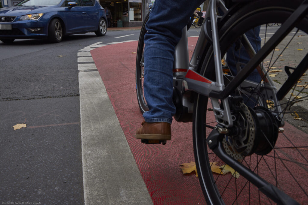Unterer Teil eines Fahrrads sichtbar, fährt auf rot markiertem Radstreifen