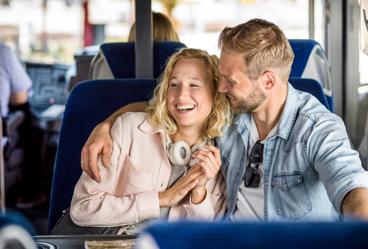 Frau sitz mit ihrem Partner im Bus und wird von ihm umarmt