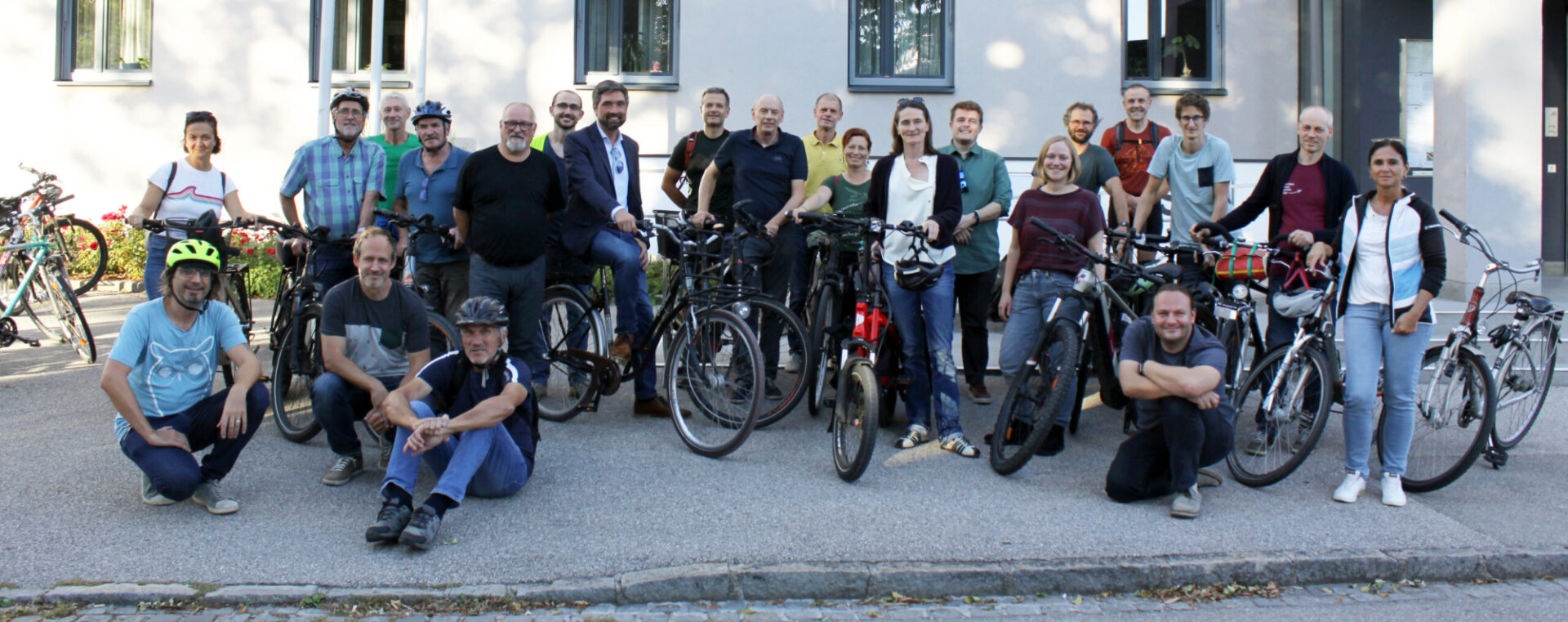 Gruppenfoto mit Fahrrädern auf einem Gehsteig, manche Personen auf dem Boden sitzend