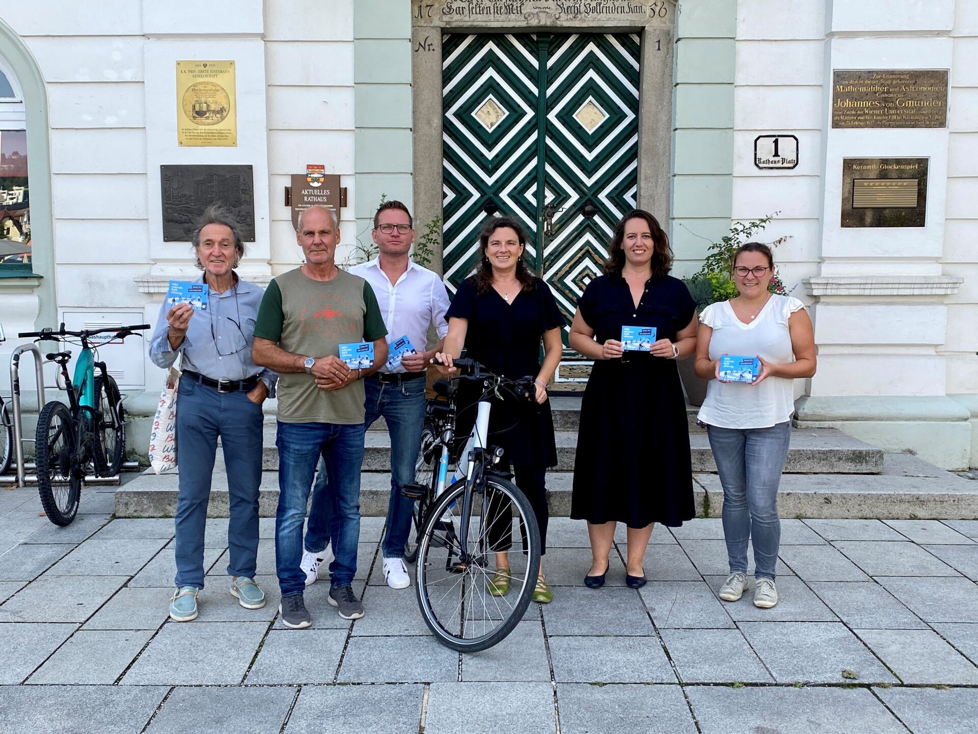sechs Personen, ein Fahrrad in der Mitte, vor einem Gebäude