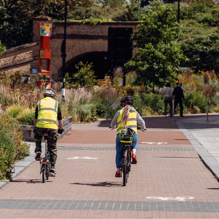 zwei Radfahrer:innen von hinten mit Warnwesten, fahren auf einem Radstreifen