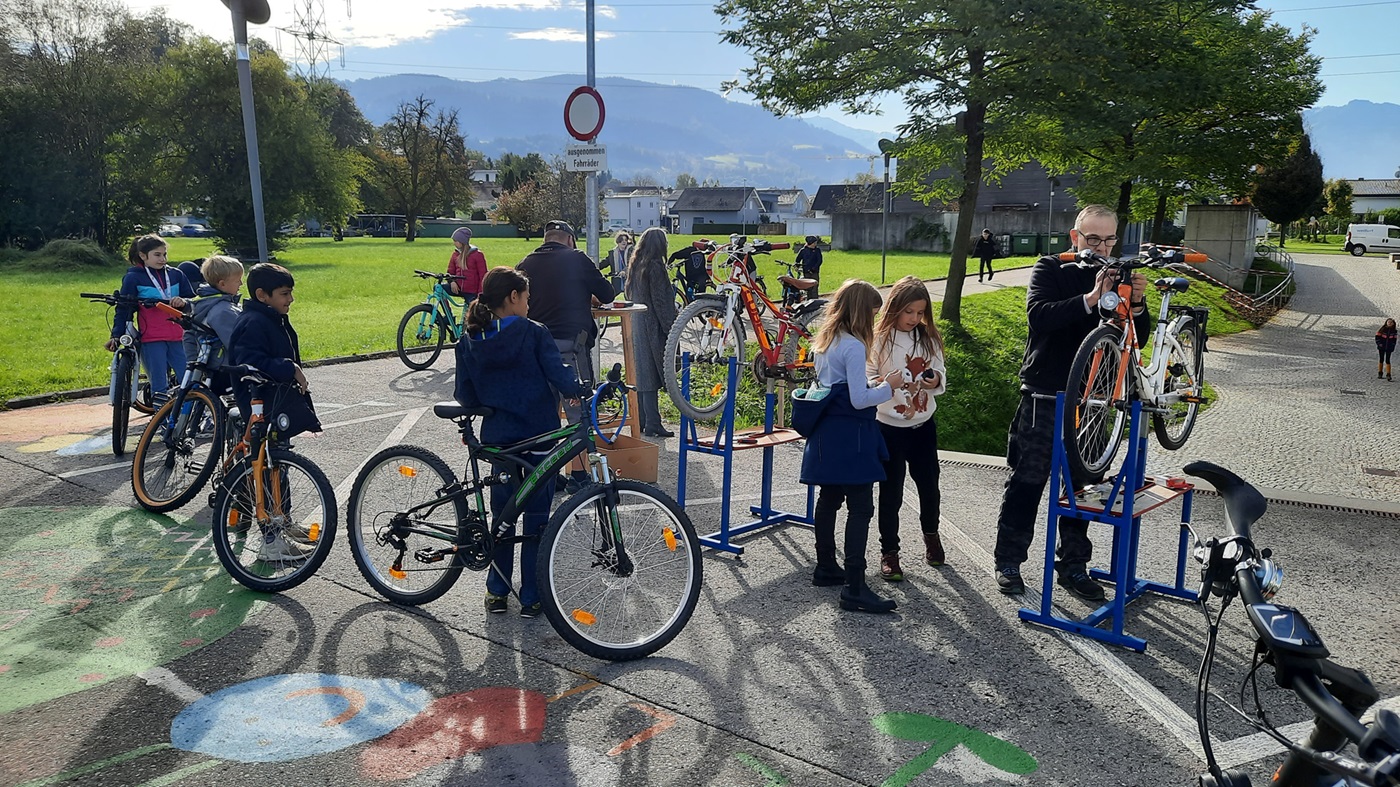 Kinder stellen sich mit ihren Fahrrädern zum Rad-Reparatur-Service an, zwei Fahrräder sind schon auf den Reparaturständern