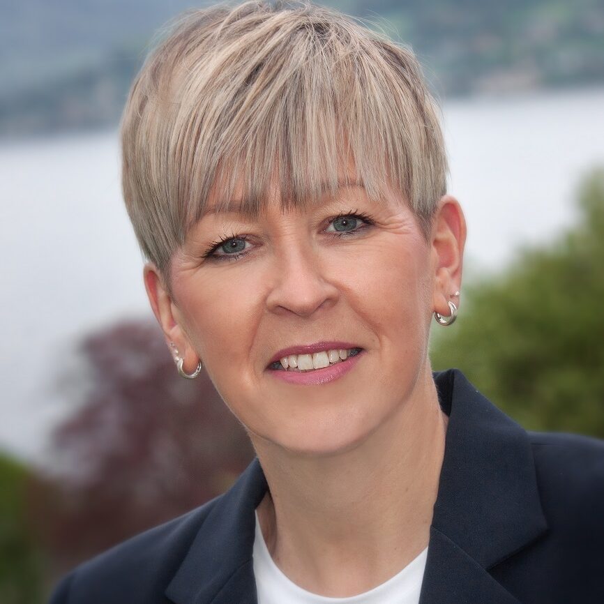 Frau mit Kurzhaarfrisur in Blazer, im Hintergrund ein See