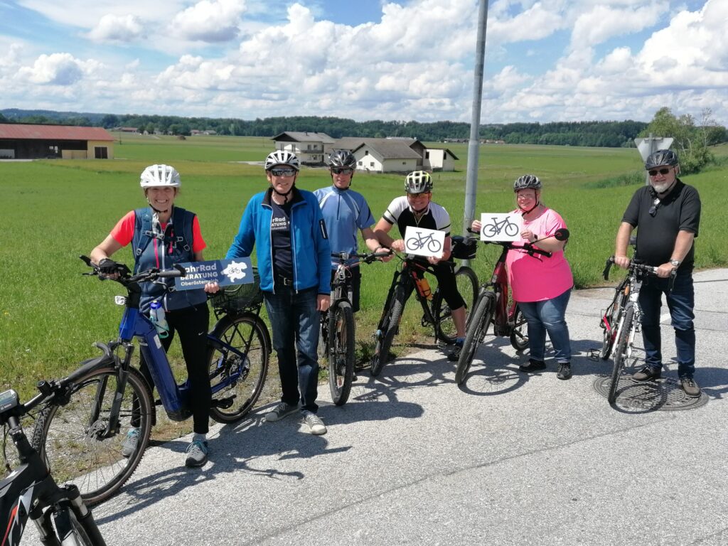 Gruppe von Radfahrenden vor flacher agrarisch geprägter Landschaft
