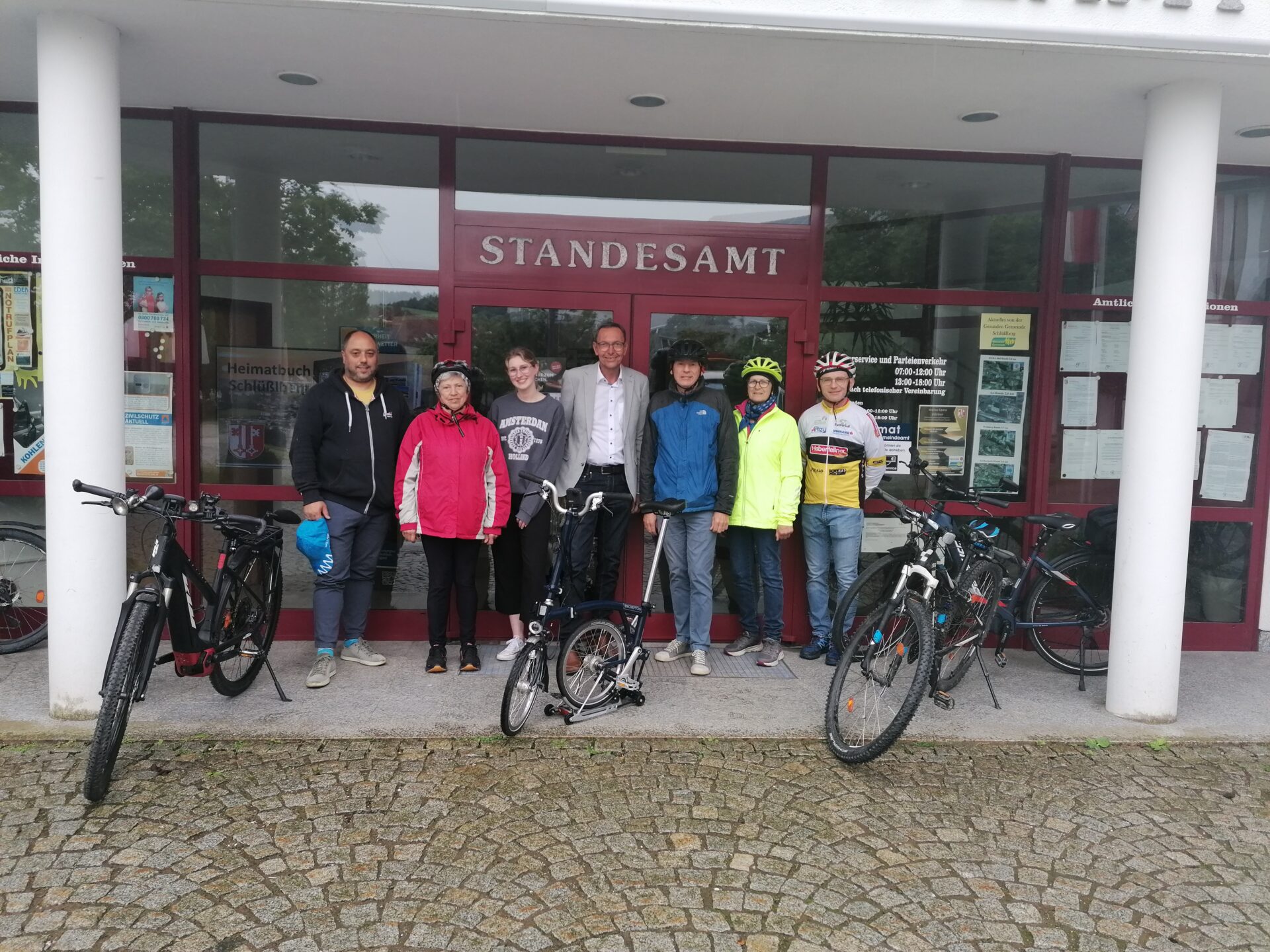 sieben Radfahrer:innen vor einem Standesamt, vor ihnen ihre Fahrräder