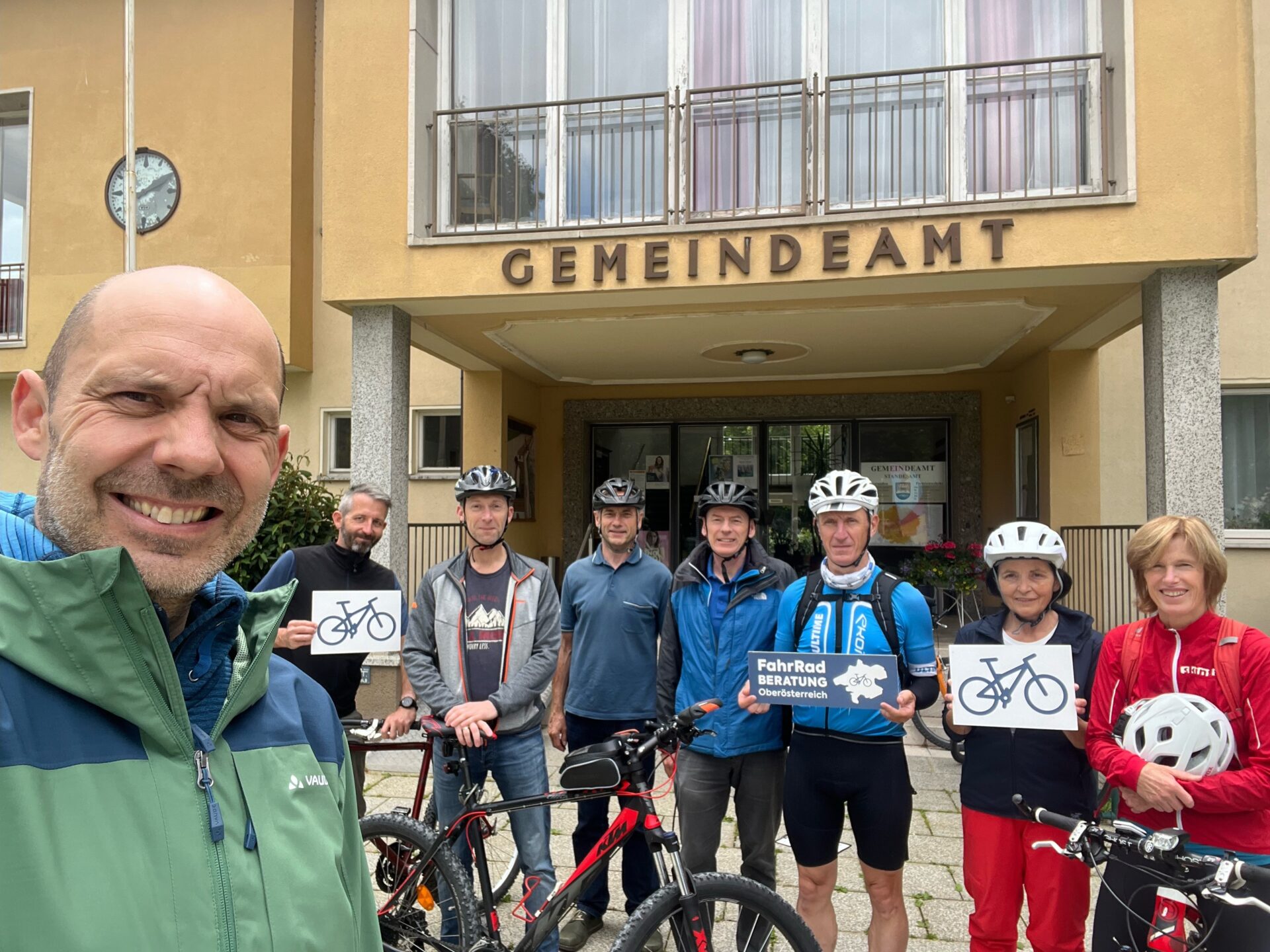 Gruppenfoto mit Fahrradhelmen, Schildern und einem Fahrrad vor dem Gemeindeamt