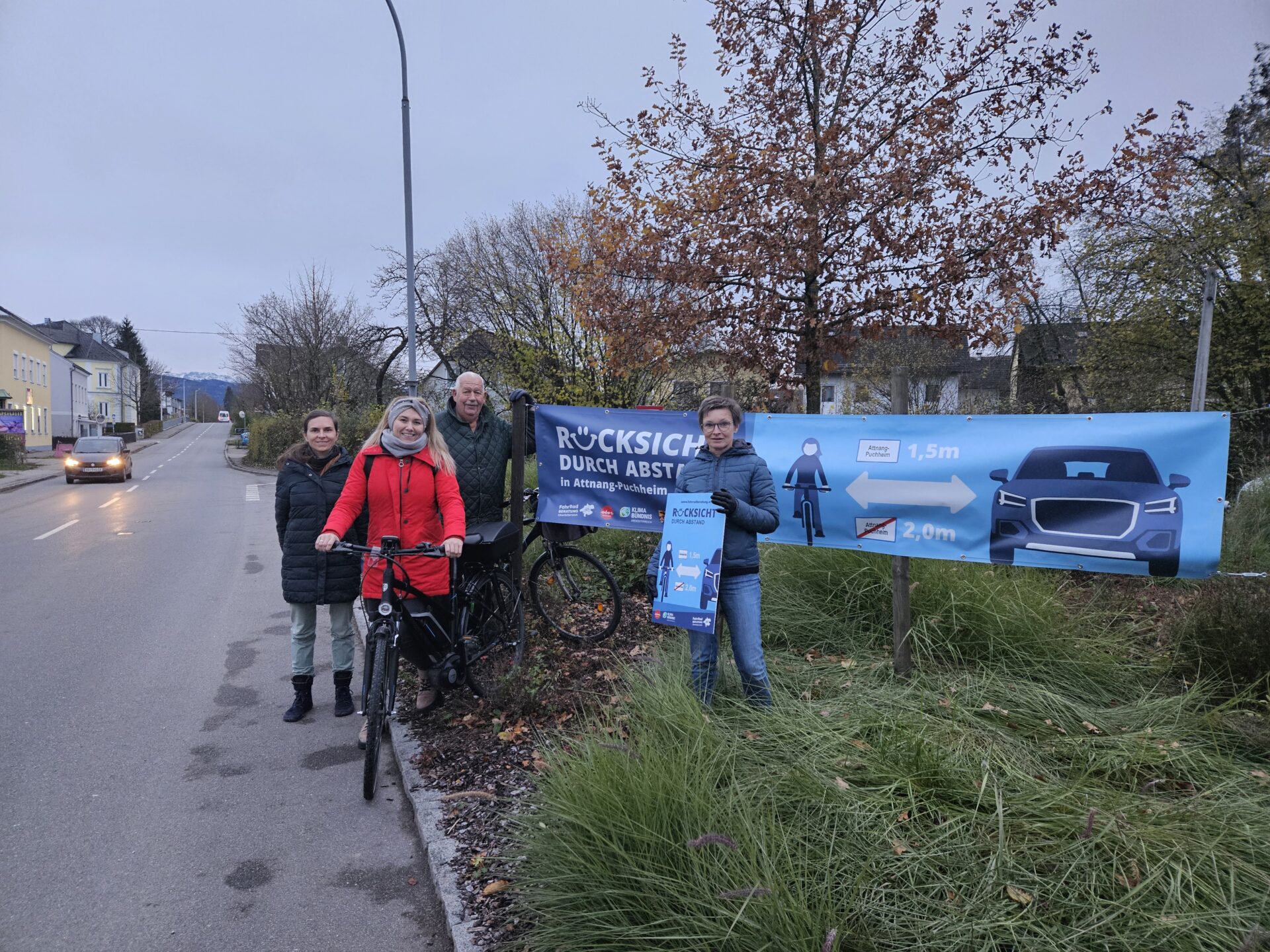 4 Personen, eine davon mit Fahrrad, ein Abstandsbanner