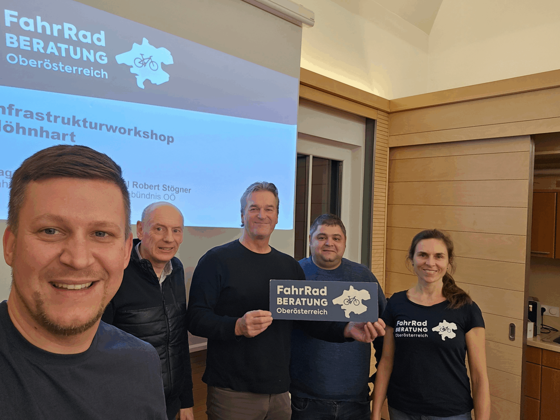 Fünf Personen posieren vor einer Präsentation zur „FahrRad Beratung Oberösterreich“, eine hält ein Schild in die Kamera.